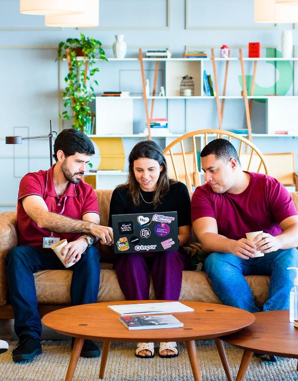 Colaboradores ímpar sentados no sofá olhando para a tela do notebook discutindo sobre o sistema.